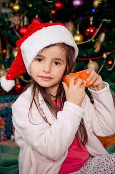Cute little girl sitting in front of christmas tree
