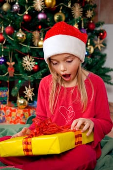 Surprised little girl holding her gift in front of christmas tree