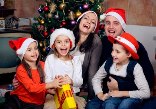 Happy family sitting in front of christmas tree. Celebrating Christmas.
