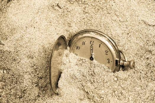 Old pocket watch lying in sand. Time concept.