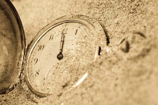 Old pocket watch lying in sand. Time concept.