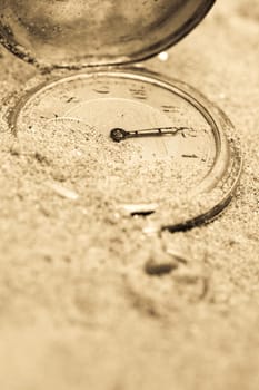 Old pocket watch lying in sand. Time concept.