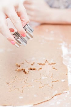 Closeup of hand of young girl making star shaped gingerbread biscuits with metal cutter from dough