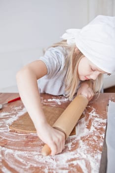 Young girl working on dough with rolling pin to make gingerbread biscuits