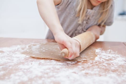 Young girl working on dough with rolling pin to make gingerbread biscuits