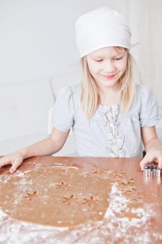 Happy young girl working with dough and shape cutters to make gingerbread biscuits