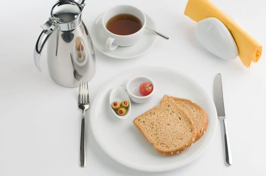 Breakfast table with thermos cup and white china, olive, tomato and bread