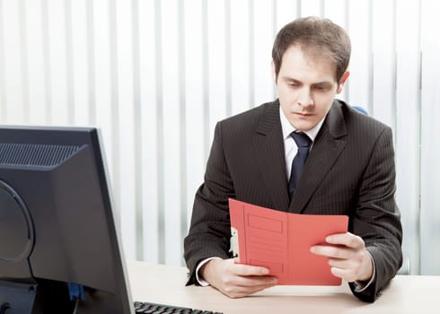 Young worried businessman reading a document at his desk, in his office