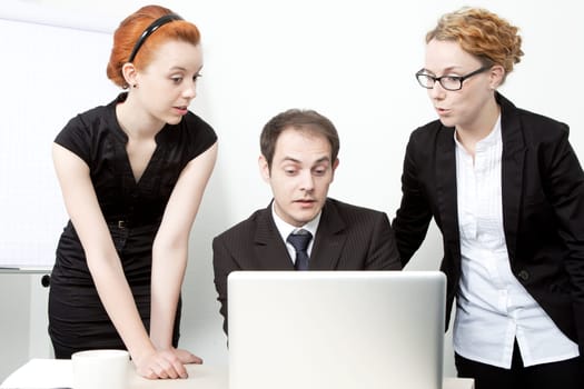 Surprised business team consisting of two women and a man gathered around a laptop computer reacting in surprise to data on the screen