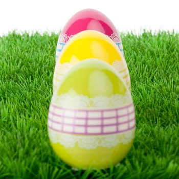 Three shiny reflective vibrant colourful Easter eggs decorated with a lacy ribbon design arranged in a receding row on green grass