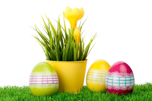 Yellow crocus flower in a yellow pot with three decorated eggs.