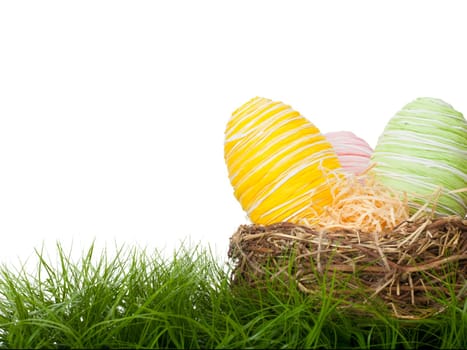 Country handcrafted Easter Eggs bound with coloured raffia straw in delicate pastel colours hidden in a straw nest on green grass for the traditional Easter Egg Hunt with copy space