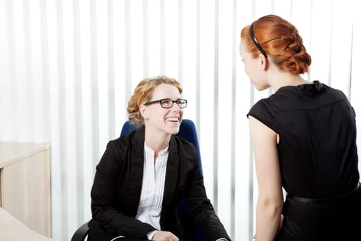 Two female business colleagues having a chat and laughing together as they share a private moment during an informal meeting in the office