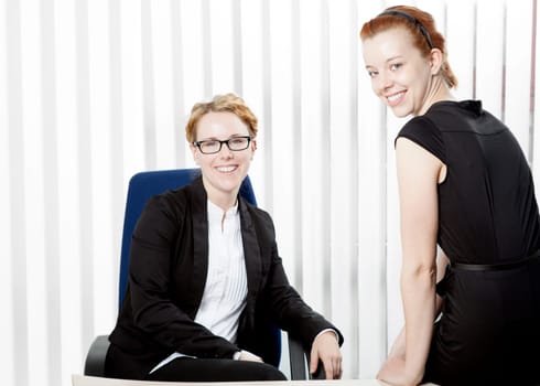 Two happy young women in an office, looking at camera