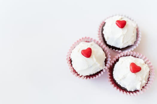 Valentine-14 February. Sweet chocolate muffins with butter cream and a red heart for decoration on a white background