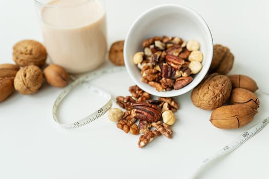 Vegan milk from nuts in a glass cup with various nuts on a white table. Nuts in a bowl. Low-calorie milk for body support