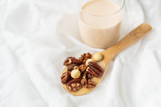 Vegan milk from nuts in a glass cup with various nuts on a white table, nuts in a wooden spoon