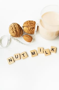 Vegan milk from nuts in a glass cup with various nuts on a white table. Lettering nut milk