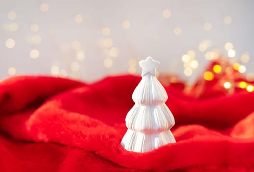 Christmas home interior with a white ceramic Christmas tree on a red blanket. Christmas and New Year concept