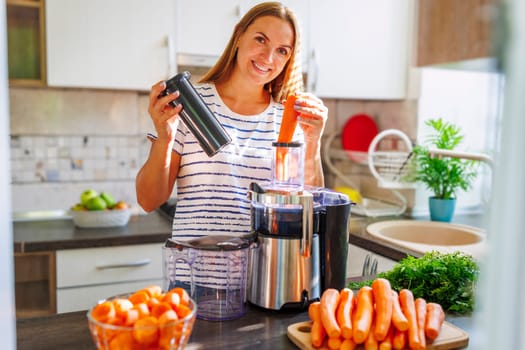 A woman making carrot juice from fresh carrots with a home juicer in the kitchen. Healthy lifestyle