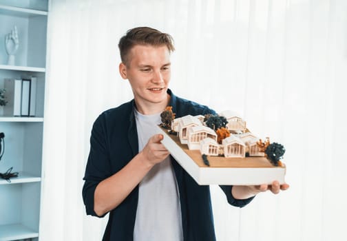 Architect designer studies elegant while holding house model, reviewing structure design for improvement with construction plan on table. Creativity and innovation in architectural design. Iteration