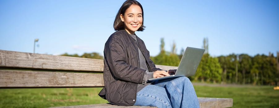 Portrait of smiling woman sitting with laptop, working on project or studying remotely, enjoying being in park.