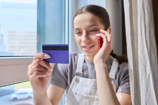 Close-up of credit bank card in hands of young teenage girl with smartphone. Online payment for goods and services, shopping, credit cards for students teenagers concept