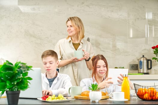 Young family with school kids have fun at breakfast time. Happy family eating healthy breakfast. Quality time with Family in kitchen eating together. Family Using Digital Devices At Breakfast