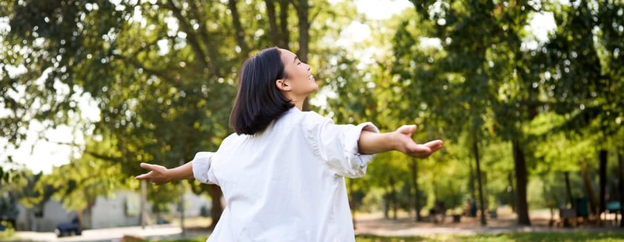 Portrait of carefree young asian woman dancing in park alone, enjoying freedom, smiling with joy. Copy space