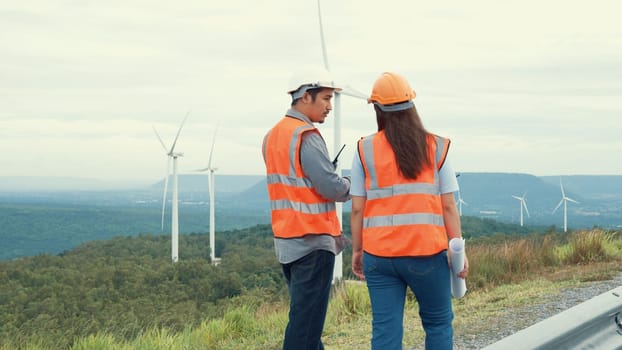 Male and female engineers working on a wind farm atop a hill or mountain in the rural. Progressive ideal for the future production of renewable, sustainable energy.