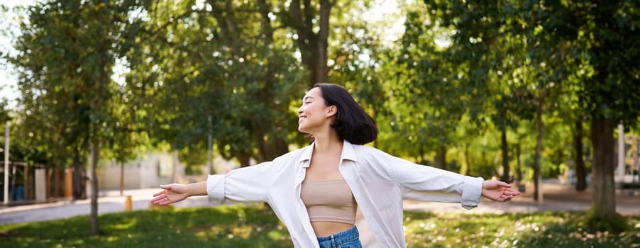 Freedom and people concept. Happy young asian woman dancing in park around trees, smiling and enjoying herself.