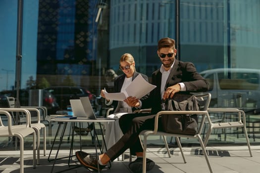 Two business partners working with documents sitting outside of office on cafe terrace