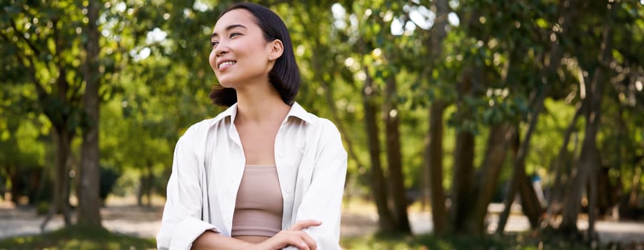 Image of korean girl walking in park, smiling while having a mindful walk in woods.