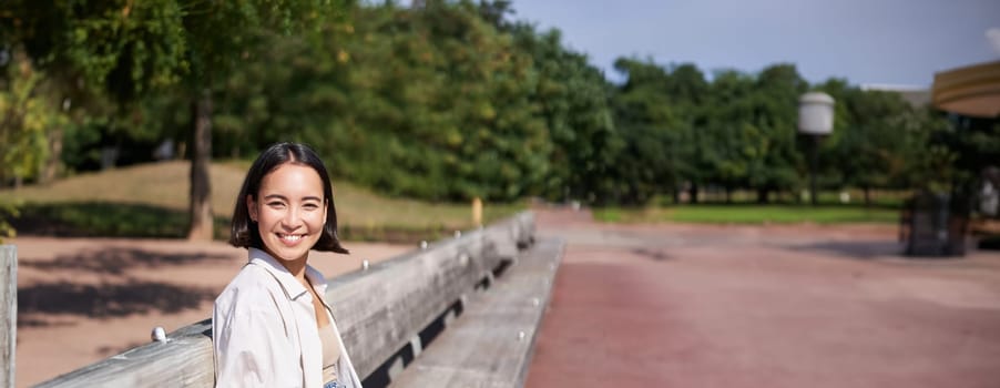 Portrait of young artist, asian girl drawing in digital tablet with graphic pen, sitting outdoors in park, getting inspiration.