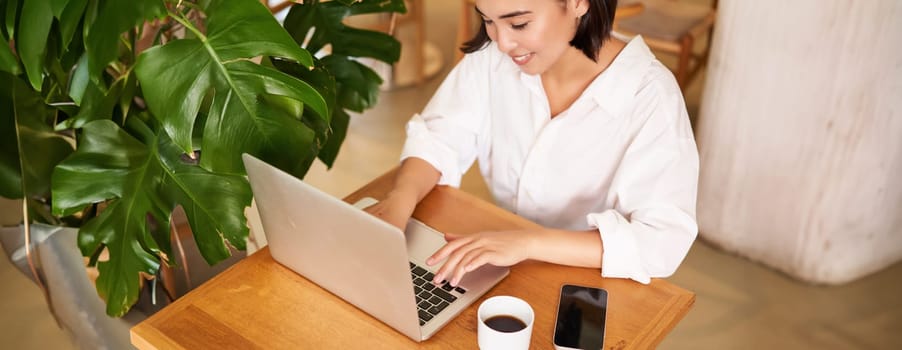 Working woman in cafe, using laptop, studying remotely, freelancing from restaurant, drinking coffee.