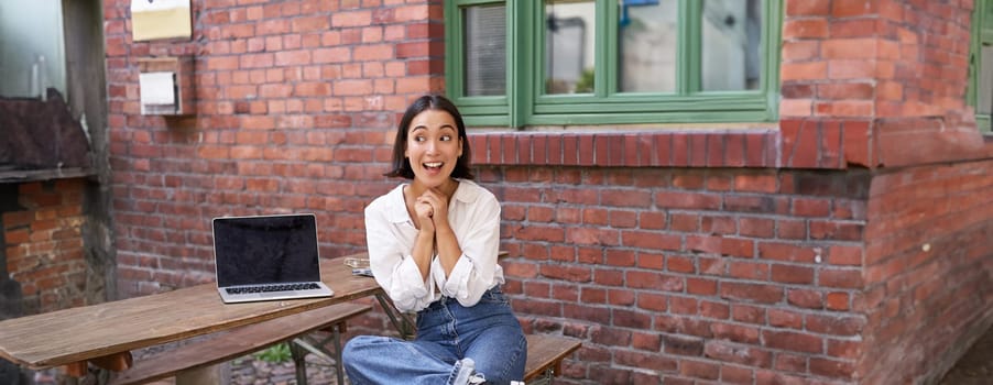 Beautiful asian woman with laptop, sitting and working in cafe, laughing and smiling, drinking coffee. Urban lifestyle and people concept