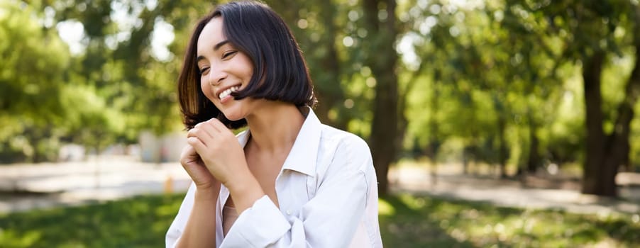 People lifestyle. Portrait of young brunette woman dancing, smiling and laughing, walking in park with hands lift up high, enjoying summer day outside.