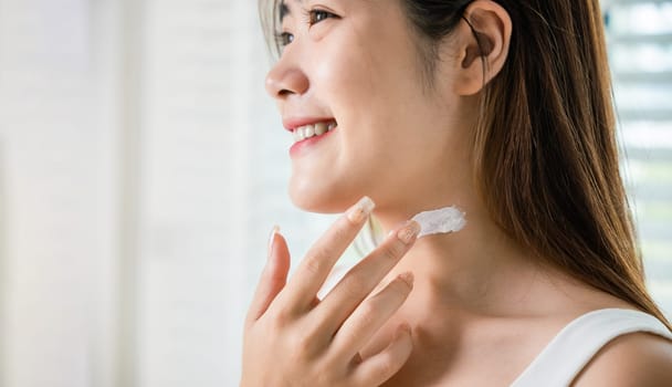 Asian beautiful young woman applying cosmetic cream on neck at home, Happy female apply lotion moisturizer on her neck after shower, Beauty skin care cosmetic protect and nourish skin concept