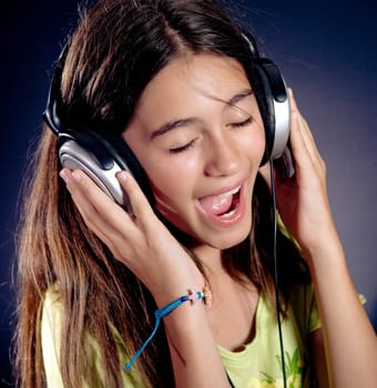 Cute girl with headphones singing. Dark background.