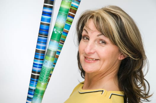 Torso shot of middle-aged woman,yellow sweatshirt and colorful rolls of wrapping paper against light studio background