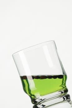 Studio shot of an angled glass with green liquid against a white background