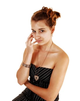 A pretty and young woman in a black dress with stripes on sitting from the side for white background.