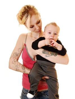 A young baby boy in the arms of his mother, a blond woman with tattoo on her body, standing in the studio for white background.
