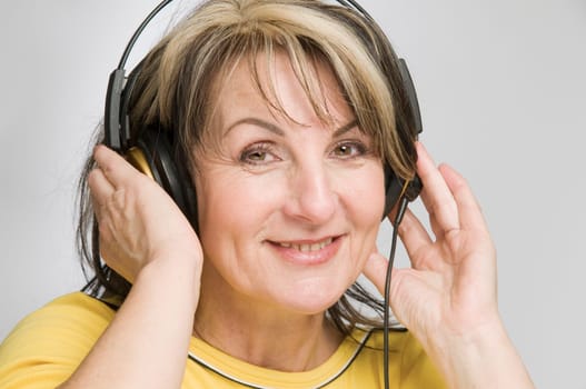 Head and shoulders shot of middle-aged woman with headphones enjoying music and sounds against white background