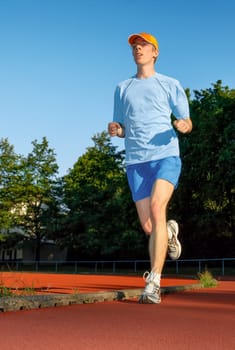 Man running on a track,with trees and blue sky in the background
