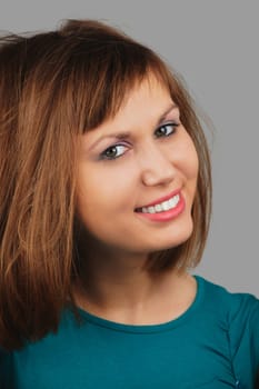 Casual young woman looking at you with a smile against a gray background