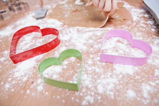 Closeup of heart shaped gingerbread biscuit cutters and hand of child preparing dough