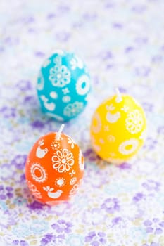 Closeup of three colorful Easter egg shaped candles on patterned surface