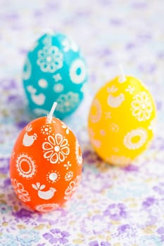 Closeup of three colorful Easter egg shaped candles on patterned surface