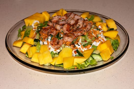 Glass plate with salad of greens, mango and shrimp
